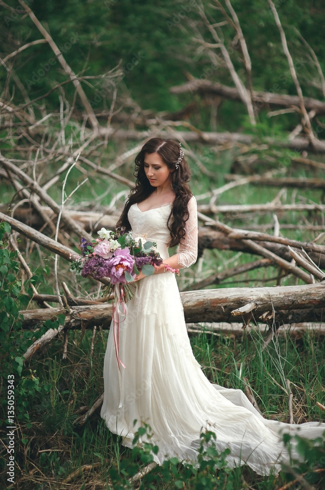 Beautiful bride in the forest with a large bouquet of different flowers. Rustic style