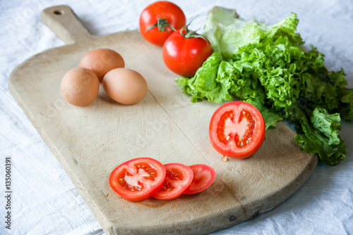 red tomatoes, lettuce, eggs, on the old wooden background. process for preparing a vegetarian breakfast.
