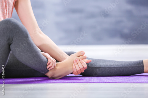 Foto Young woman suffering from pain in foot while sitting on stretching mat, close u