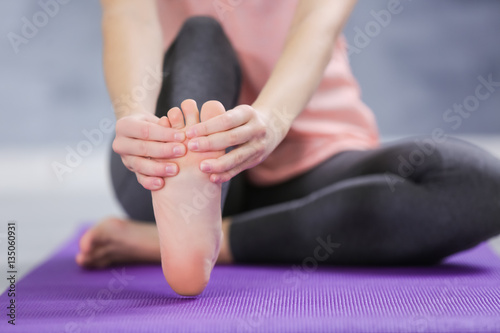 Young woman suffering from pain in foot while sitting on stretching mat, close up