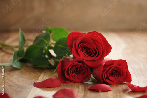 three red roses and petals on old wood table with copy space  romantic background