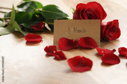 Fototapeta Naklejka Na Ścianę i Meble -  three red roses and petals on old wood table with 8 march paper card, romantic background