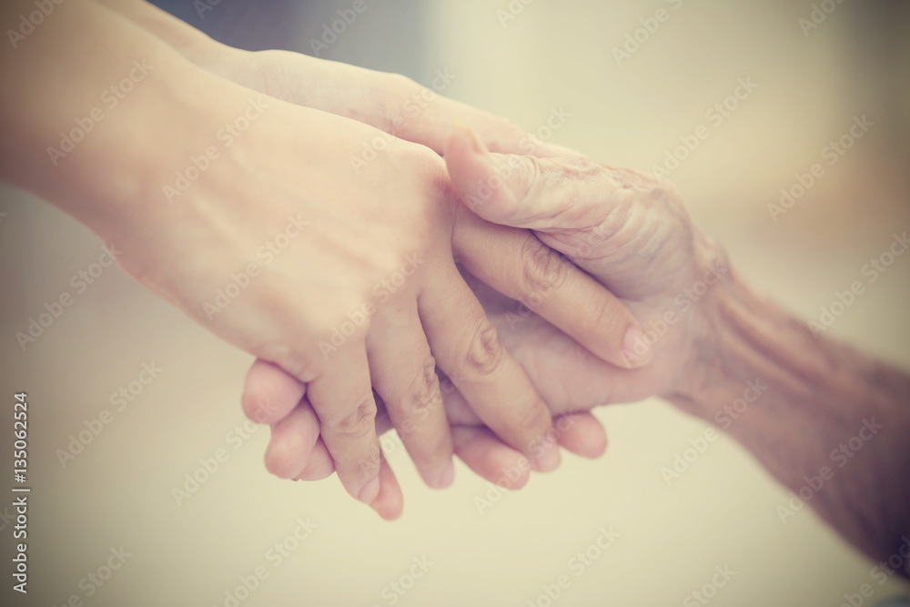 Old and young holding hands on light background, vintage tone. Old and young holding hands on light background, vintage tone.