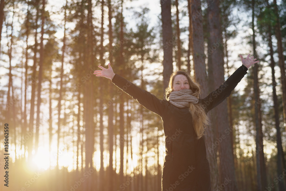 teen girl raised hands in winter pine forest in sunset, freedom or victory concept