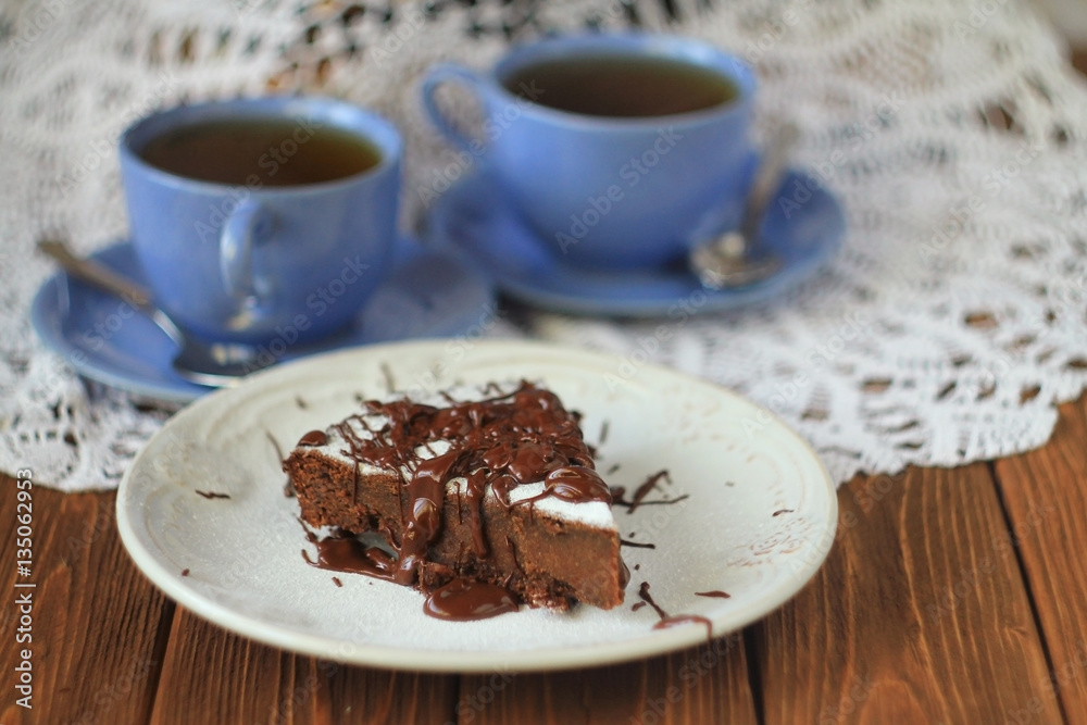 two cups of tea and a piece of chocolate cake on a table with a white lace tablecloth two cups of tea and a piece of chocolate cake on a table with a white lace tablecloth