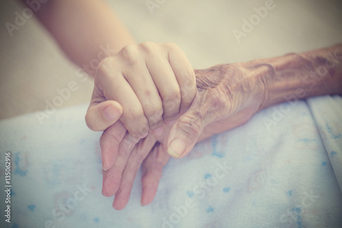 Old and young holding hands on light background, vintage tone.