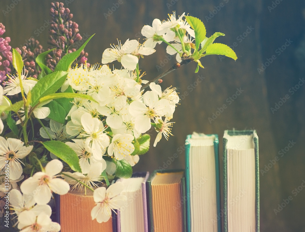 Fototapeta premium Pile of books and spring flowers of a lilac and apricot on a wooden background.