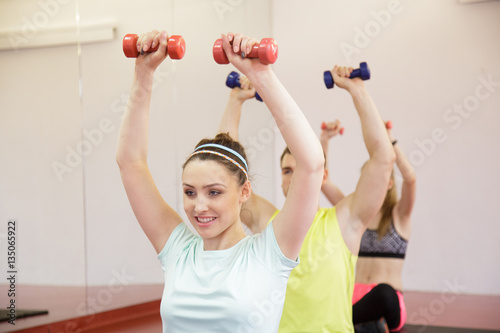 Group of smiling people working out with dumbbells in gym
