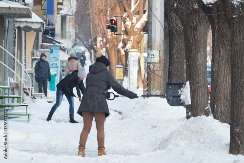 Business woman with shovel cleaning snow filled street in front of the office at work