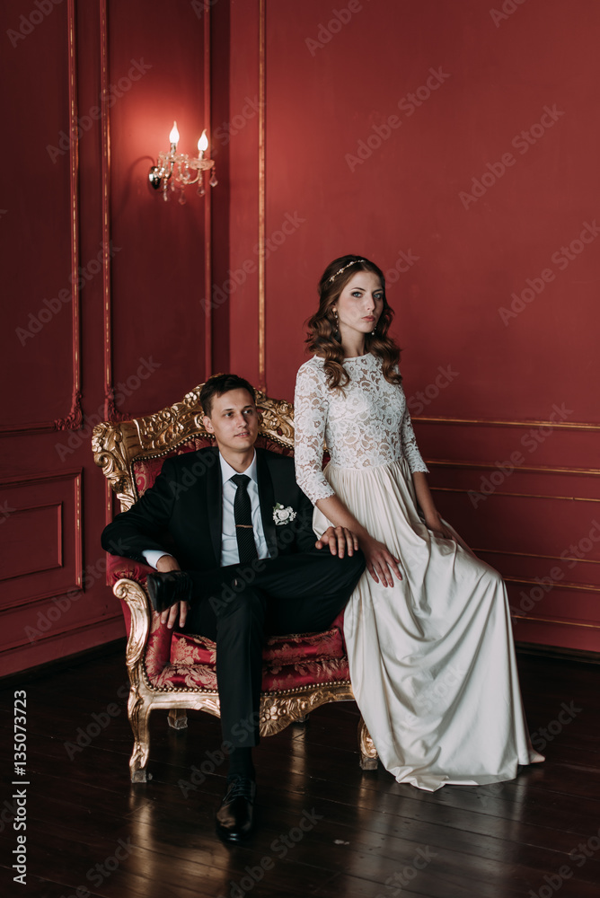 cute wedding couple in the interior of a classic studio with red background . hey kiss and hug each other, holding hands looking at each other