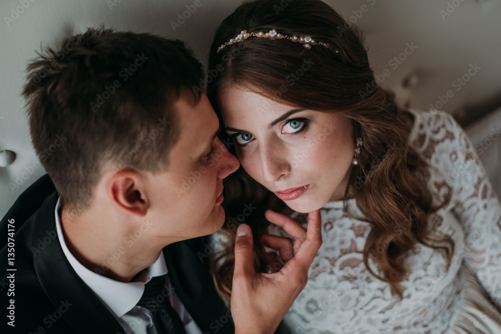 cute wedding couple in the interior of a classic white studio decorated. hey kiss and hug each other, holding hands looking at each other