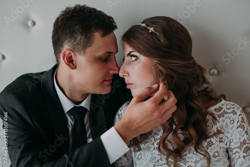 cute wedding couple in the interior of a classic white studio decorated. hey kiss and hug each other, holding hands looking at each other © dashamuller