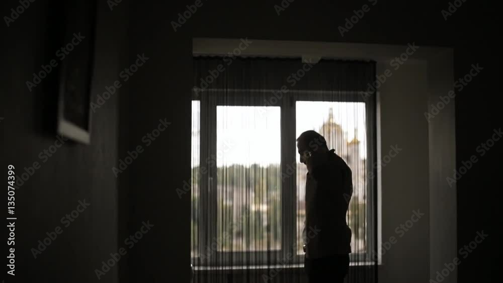 Putting a jacket silhouetted slow motion backlit. Unrecognizable man throws jacket over shoulder and buttons prepare to go out stand by window lake residence. Establishment leadership royalty success Putting a jacket silhouetted slow motion backlit. Unrecognizable man throws jacket over shoulder and buttons prepare to go out stand by window lake residence. Establishment leadership royalty success