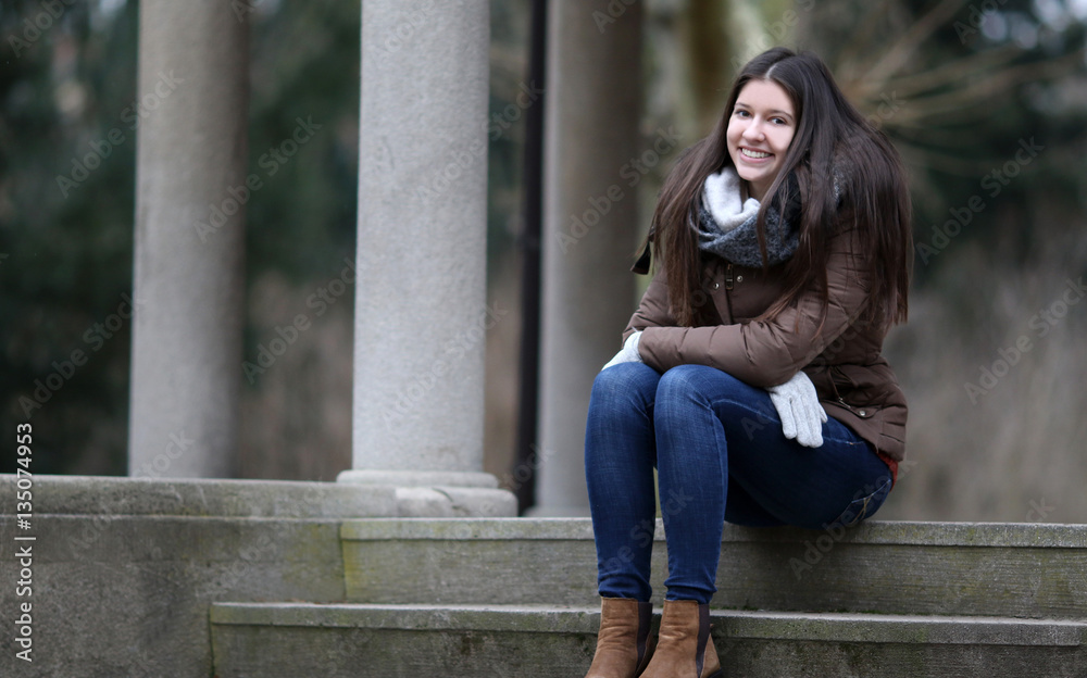 Junge modisch gekleidete Frau im Winter sitzt auf einer Steintreppe im Park