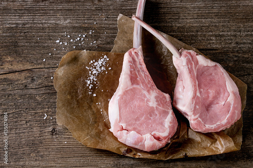 Fotografia Two raw uncooked Veal tomahawk steak with sea salt on baking paper over old wooden background