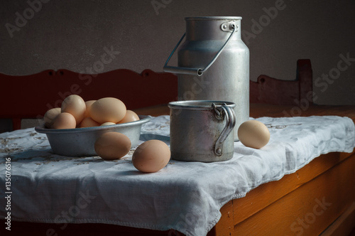 Still life in a rustic style: set of aluminum cookware and eggs on a wooden table. Natural light from the windows.