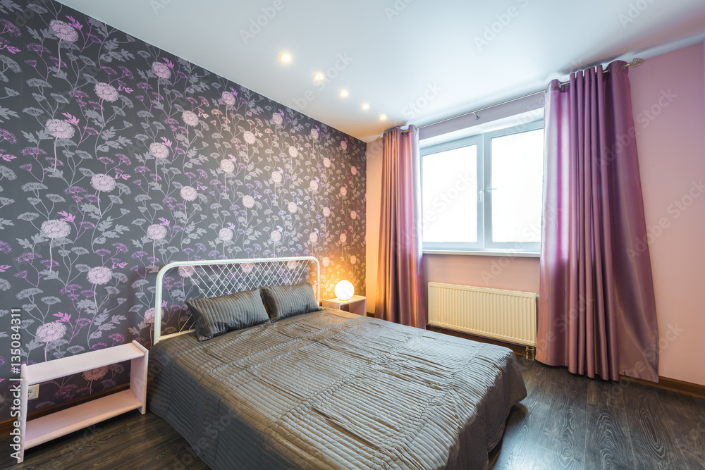 Fototapeta premium Interior bedroom with a large double bed with bedside tables, window on a background of modern wallpaper