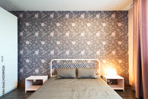 Interior bedroom with a large double bed with bedside tables on a background of modern wallpaper