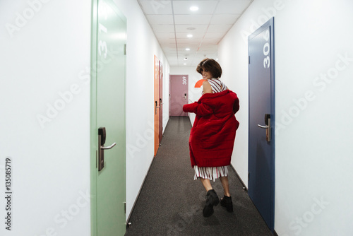 Cheerful young woman running and looking back in corridor