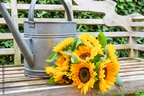 Fototapeta Naklejka Na Ścianę i Meble -  Fresh bunch of sunflowers and zinc watering can on garden bench.