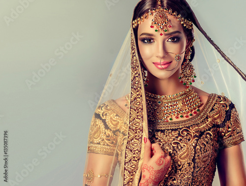 Portrait of beautiful indian girl. Young hindu woman model with golden kundan jewelry set . Traditional Indian costume lehenga choli .
