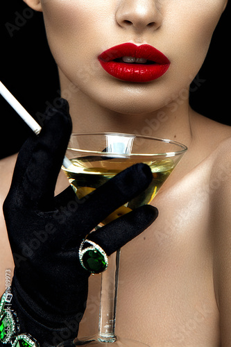 Fashion woman portrait of half face. Red lips and hand with martini and cigarette.