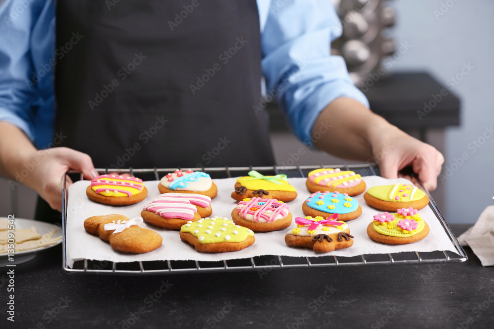 Woman holding baking grid with colourful Easter cookies, closeup Woman holding baking grid with colourful Easter cookies, closeup
