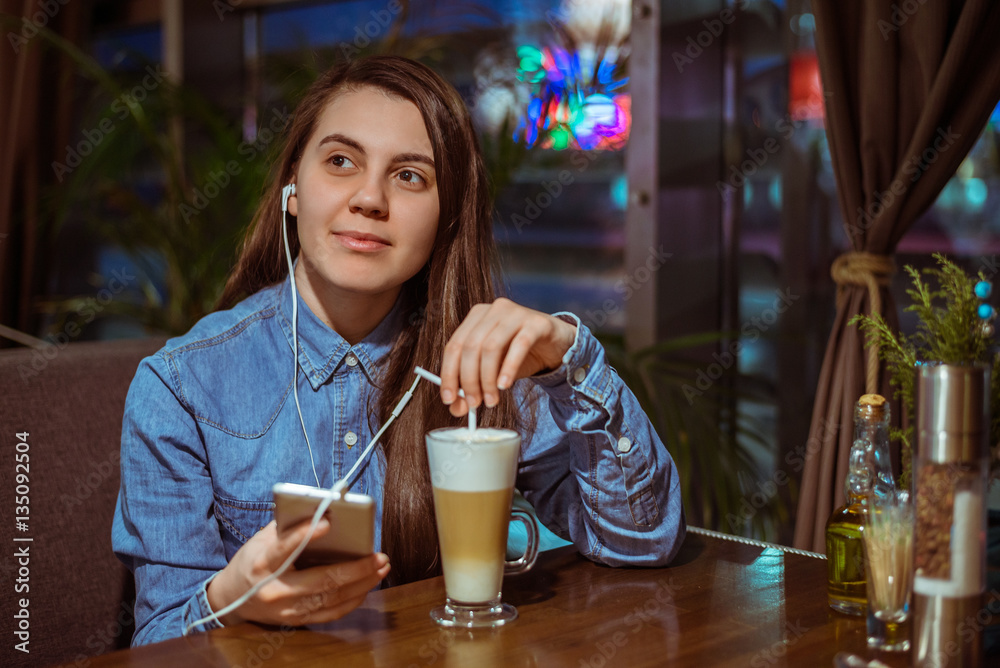Music smartphone in female hand, on cafe interior background Music smartphone in female hand, on cafe interior background