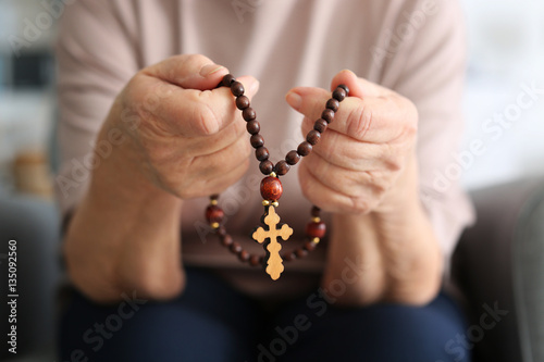 Elderly woman with rosary beads at home, closeup