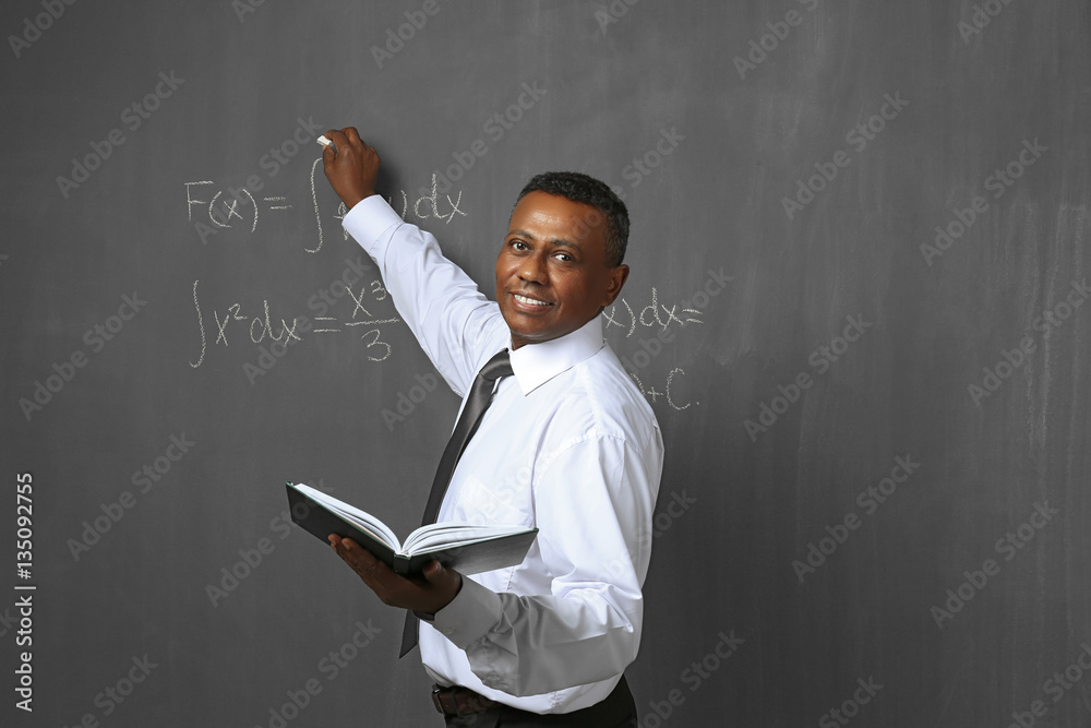 Confident indian teacher writing math formulas on blackboard stock