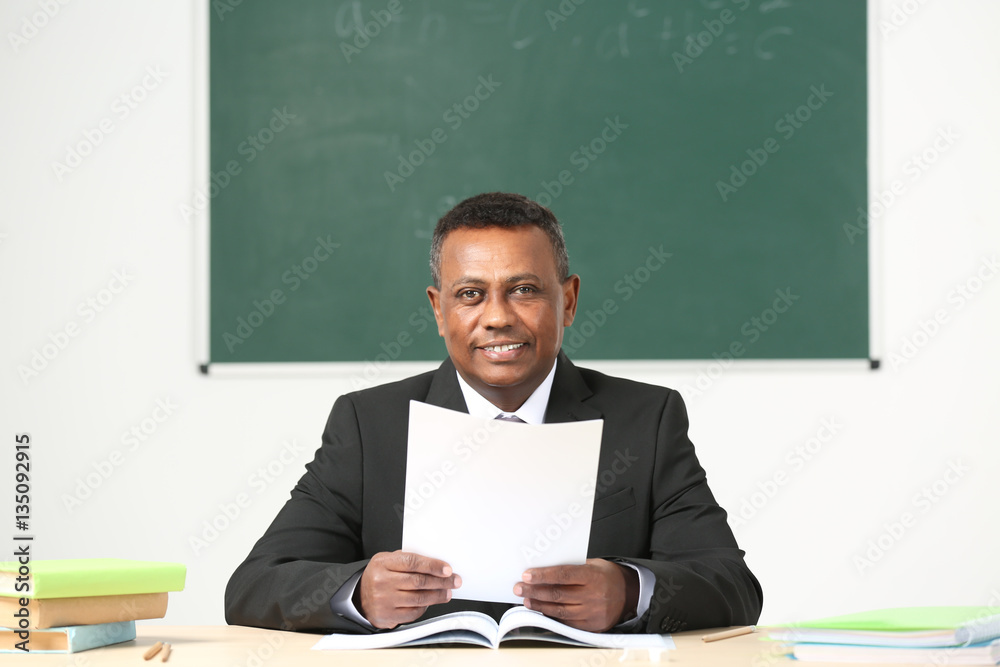 Confident Indian teacher sitting at table in classroom Confident Indian teacher sitting at table in classroom