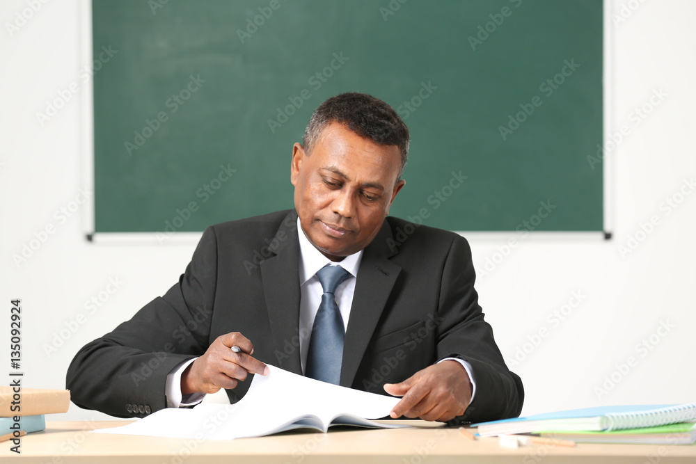 Confident Indian teacher sitting at table in classroom Confident Indian teacher sitting at table in classroom