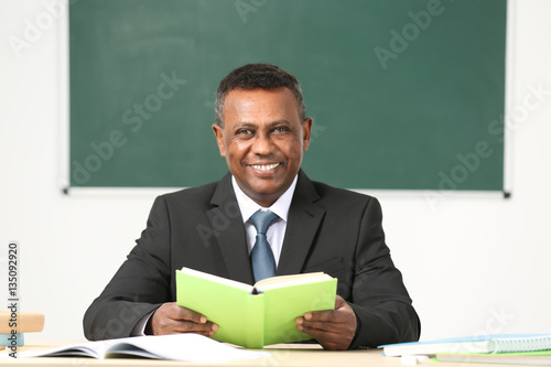 Confident Indian teacher sitting at table in classroom