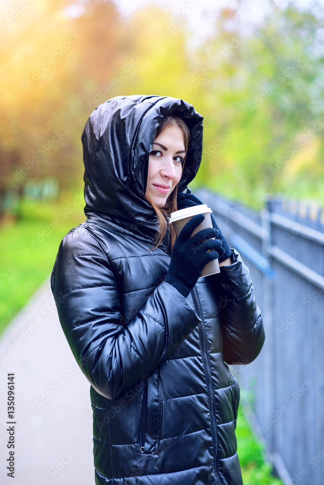 Girl in jacket with hood, holding a coffee or tea, young enjoys the outdoors and sports, spring  autumn, lifestyle, black , smiling brunette in gloves