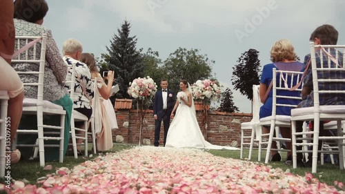 Wedding ceremony location with bride and groom, pink petals path beetwen white guests chairs photo