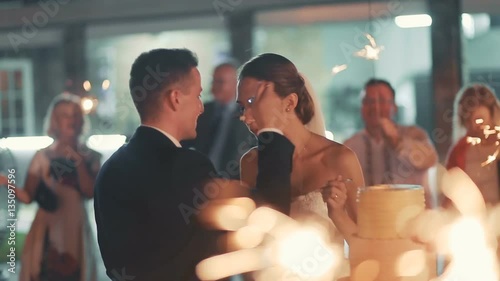 Beautiful young wedding couple eating cake, guests with sparklers