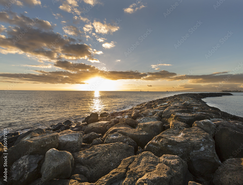 Hawaiian Sunset over a rock barrier