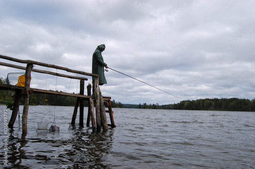 Fisherman standing on the dock in a long raincoat. He is waiting for the fish to bite.