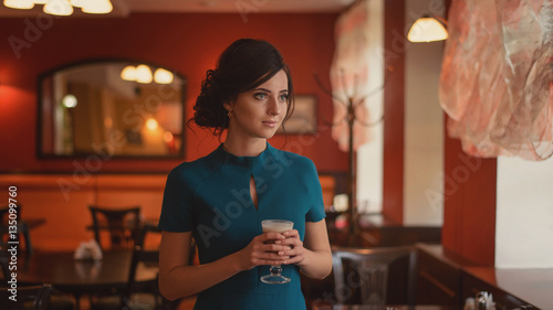 Pensive pretty girl in classic elegant dress standing at the cafe going to drink coffee.