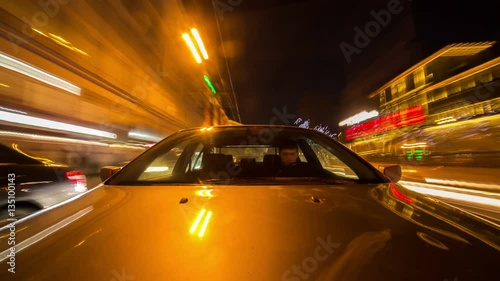 Camera mounted on car hood facing window, driving through a city downtown with vivid reflections on hood of sky, clouds and city lights.