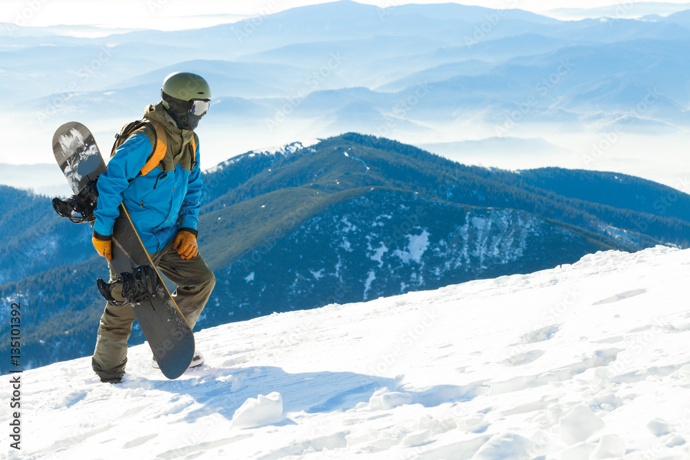 Young snowboarder in helmet walking at the top of a mountain Young snowboarder in helmet walking at the top of a mountain