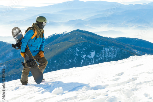 Young snowboarder in helmet walking at the top of a mountain
