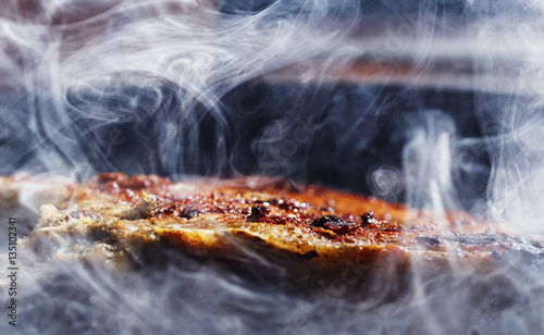 smoke and steam rise from a pork steak on grill pan