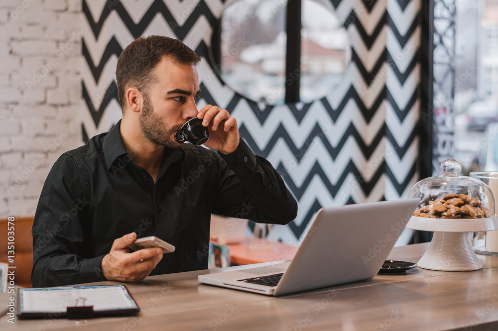 Confident young man working on laptop and drinking coffee while Confident young man working on laptop and drinking coffee while