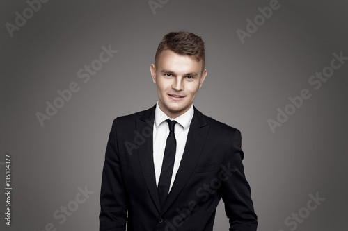 Young trendy man. Black suite and tie, gray background. Portrait