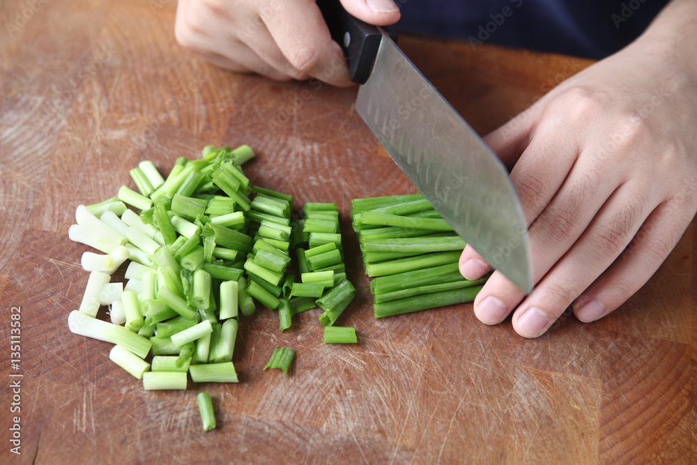 A man uses a chef’s knife to chop up scallions on a cutting board
