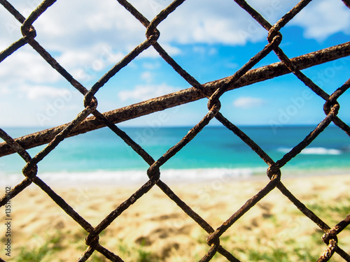 Closeup photo of a rusty old chain link fence with a beach in the background near Makaha Hawaii.