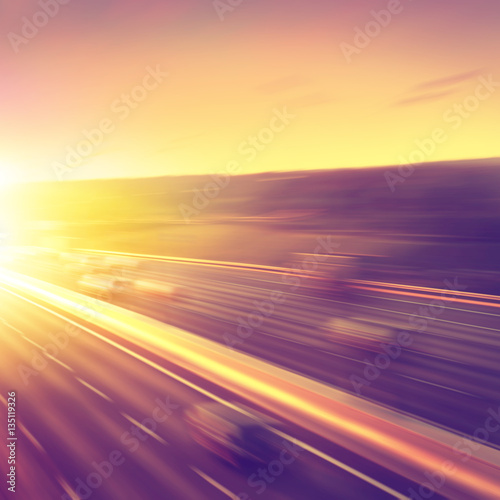 Cars in motion blur on highway during sunset.