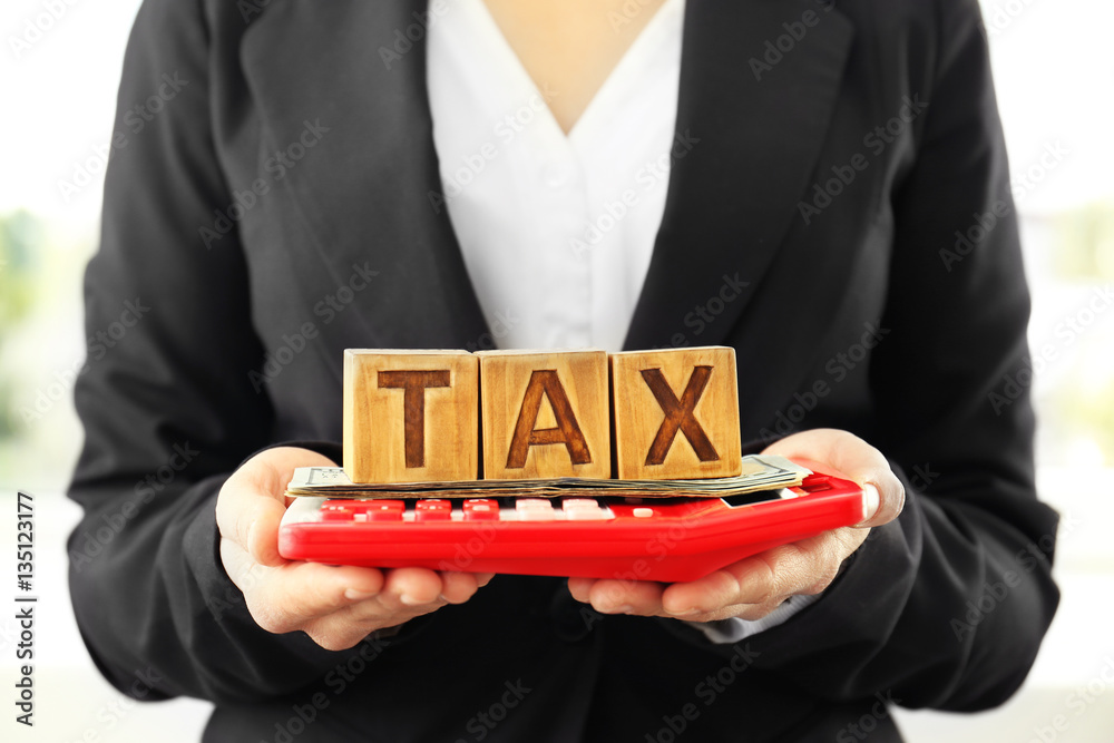 Female hands holding wooden blocks with word TAX, money and calculator, closeup Female hands holding wooden blocks with word TAX, money and calculator, closeup