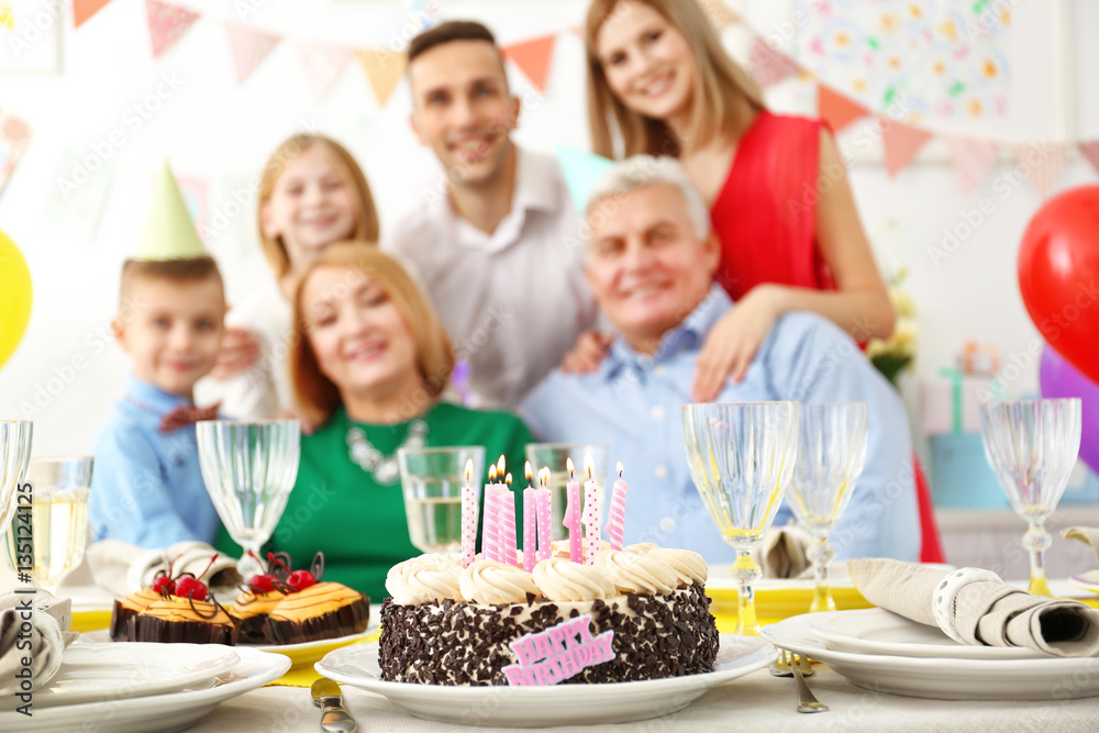 Birthday cake on table with happy family on background